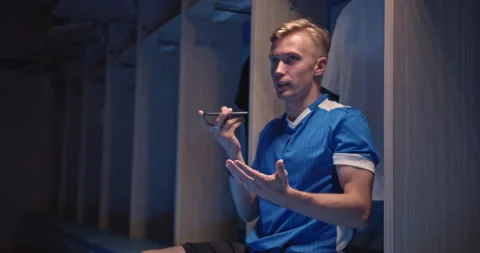Young soccer player, man talking with phone sitting in the locker room at the Stock Footage 141663768