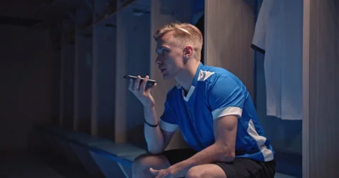 Young soccer player, man talking with phone sitting in the locker room at the Stock Footage 145799786
