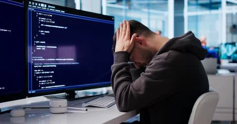 Young Software Engineer Looks Tired And Stressed While Coding At Desk. Stock Photos