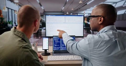 Young Software Engineer Uses Laptop And Desktop To Debug Mobile App. Foto stock