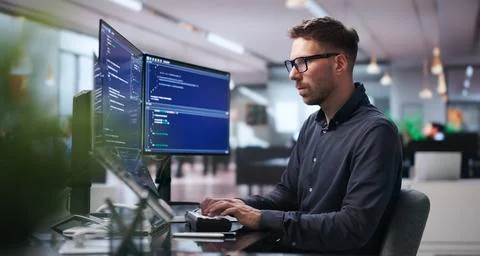 Young Software Engineer Works On Complex Algorithms Using Dual Screens At Des Stock Photos