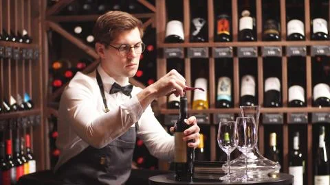 Young sommelier opens a bottle of red wine in a wine boutique for tasting Stock Photos