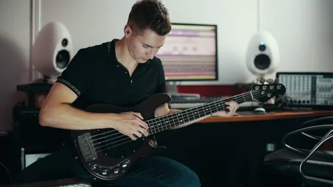 Young sound engineer trying to play on bass guitar in the studio 動画素材 305451775