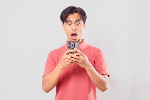 Young southeast Asian man holding smartphone with shocked expression on pla.. Stock Photos