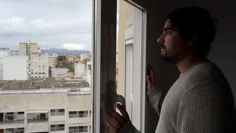 Young spanish man gets closed to the window to enjoy watching outdoors meanwh 스톡 동영상 129044222