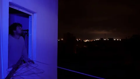 Young spanish man looks through the window during a fireworks show 스톡 동영상 129043232