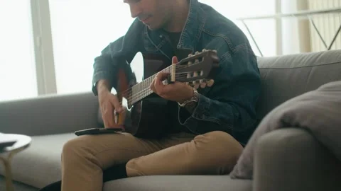 Young Spanish Man Playing Classical Guitar On Sofa At Home Stock Footage 336629587