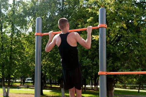 A young sports guy does pull-ups on the horizontal bar in sportswear on street Stock Photos