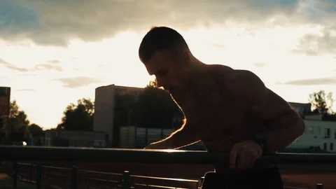 Young sportsman doing dips on parallel bars outdoors with beautiful sunset on 動画素材 120508142