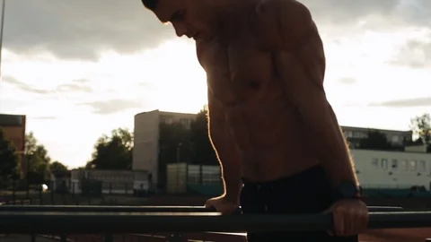 Young sportsman doing dips on parallel bars outdoors with beautiful sunset on Stock Footage 121901676