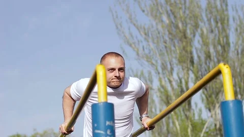 Young sportsman pushing up at the parallel bars in sunny day. Street workout. Stock-Footage 75081380