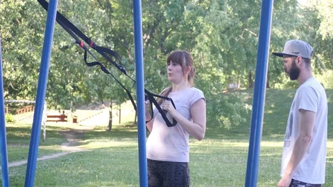 Young sportswoman making pull-ups on fitness loops under control of bearded Video stock 99206718
