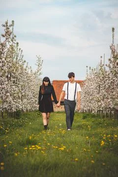 Young strong love between two young people walking under apple trees. Candid  Stock Photos