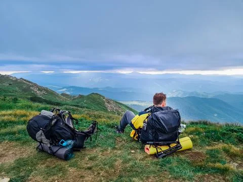 Young strong man with backpack sitting on the ground resting after climbing u Stock Photos