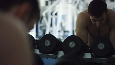 Young strong man looking in a mirror near dumbbells in a gym Vídeos de archivo 105941247