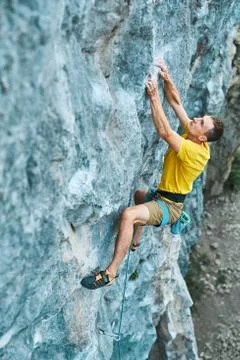 Young strong man rock climber in yellow t-shirt, climbing on a cliff Stock Photos
