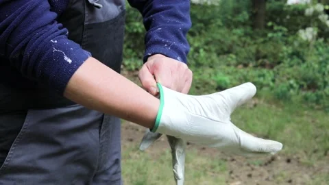 Young strong man in work overall is putting his garden gloves on in the garden Stock Footage 130654451
