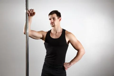 Young strong pole dancer smiling man in black clothes on pylon. White backgro Stock Photos