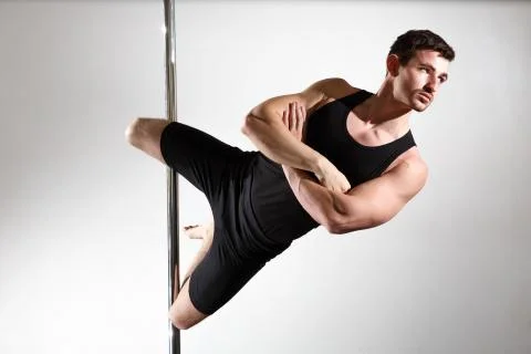 Young strong pole dancer smiling man in black clothes on pylon. White backgro Stock Photos