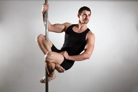 Young strong pole dancer smiling man in black clothes on pylon. White backgro Stock Photos