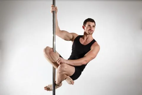 Young strong pole dancer smiling man in black clothes on pylon. White backgro Stock Photos