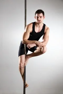 Young strong pole dancer smiling man in black clothes on pylon. White backgro Stock Photos