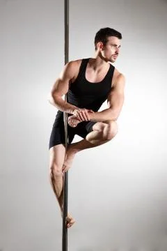 Young strong pole dancer smiling man in black clothes on pylon. White backgro Stock Photos