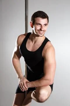 Young strong pole dancer smiling man in black clothes on pylon. White backgro Stock Photos