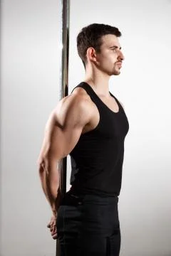 Young strong pole dancer smiling man in black clothes on pylon. White backgro Stock Photos
