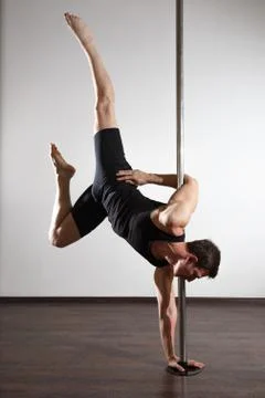 Young strong pole dancer smiling man in black clothes on pylon. White backgro Stock Photos