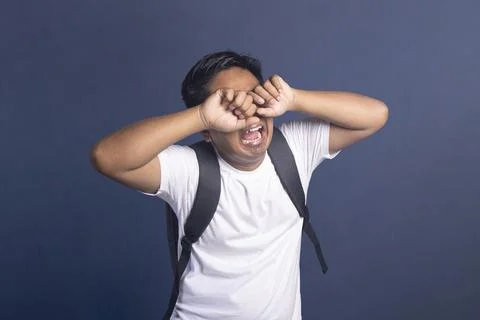 Young student with a backpack crying and rubbing his eyes with both hands i.. Stock Photos