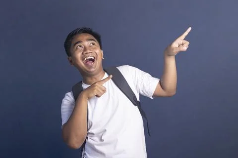 Young student with a backpack pointing up with an excited and happy facial .. Stock Photos