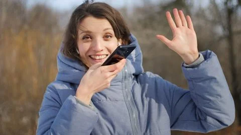 Young student in blue coat is using her smartphone to send a voice message to a Foto stock
