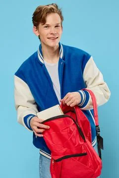 A young student in a bomber jacket takes out a notebook from his backpack Stock Photos