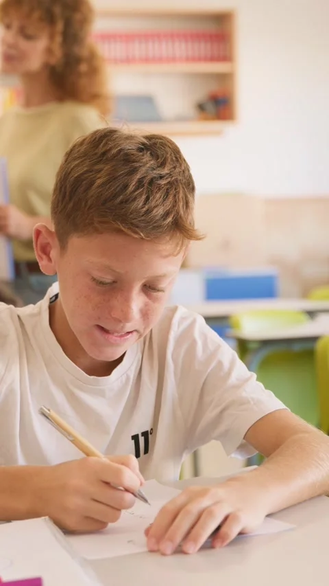 Young student doing his homework in class with teacher watching Video stock 345113625