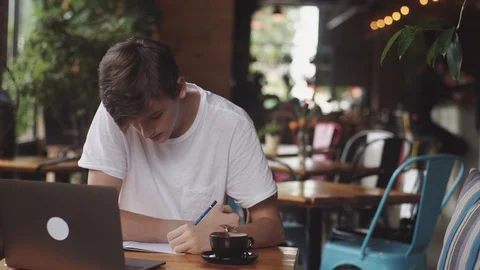 Young student doing homework in cafe, freelancer using pencil to draw on paper 스톡 동영상 112594595