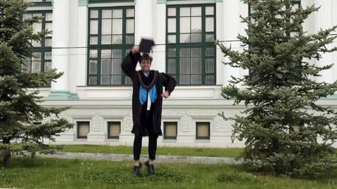 Young student dressed in black robe happy and enthusiastically jumps up and Stock Footage 316091599