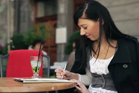 Young student drinking cocktail and writing notes in cafe NTSC Video stock 11137578