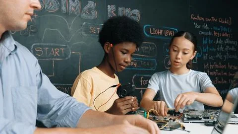 Young student fixing controller while teacher programing code. Edification. Stock Photos