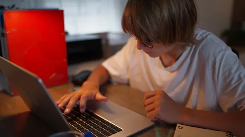 Young student focused on schoolwork at home using a laptop and notebook. Ac.. Stock Footage 341977331