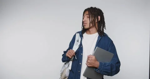Young student gazes upward while holding laptop and backpack in a bright in.. Stock Footage 313951110