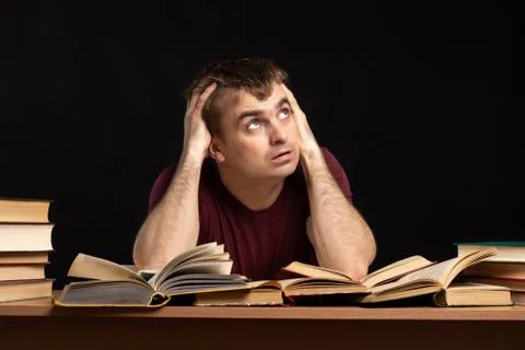 Young student guy sitting at a table with books with a tired look Stock Photos