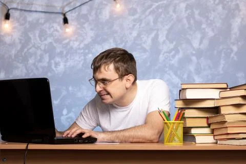 Young student looking at a laptop while sitting at a desk with books and papers. Stock Photos