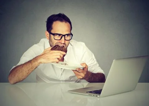 Young student man eating while working on laptop Stock Photos