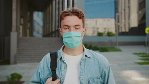 Young student in a mask look at camera hold books. Stand on street near Stock Footage 142048809
