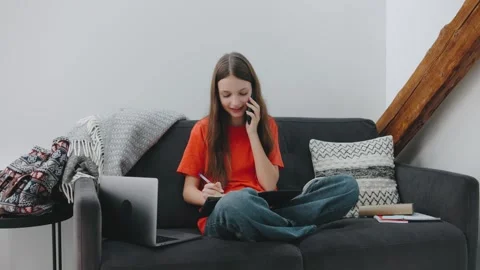 Young student multitasking at home, reviewing notes, writing, and on a phone Stock Footage 305772570