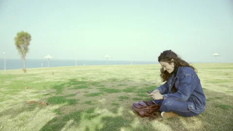 Young student is in the park by the sea on a sunny day and types a message Stock Footage