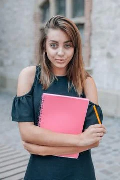 Young student is posing in front of the camera and holding pen and notepad in Stock Photos