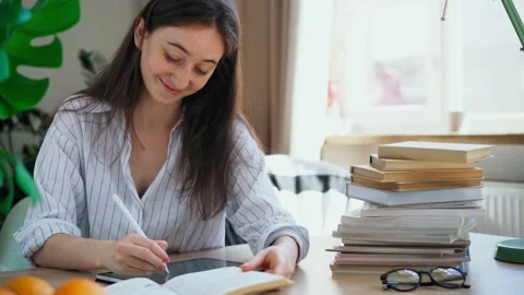 Young student preparing for exams rewrites a lecture from a book into a tablet Stock Footage 155959282