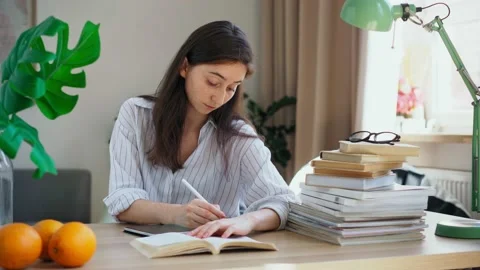 Young student preparing for exams rewrites a lecture from a book into a tablet Stock Footage 156018722